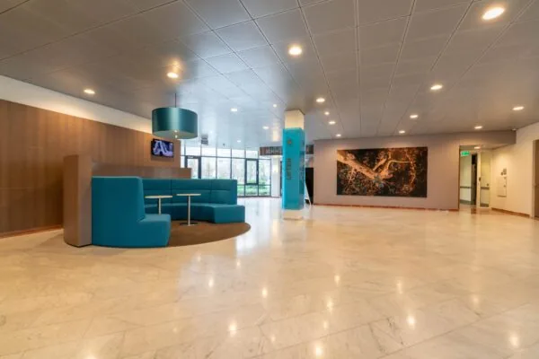 Moderne ontvangsthal aan de De Bruyn Kopsstraat met turquoise zitgedeelte, kunst aan de muur en marmeren vloer.